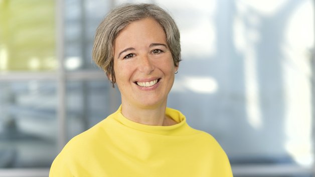 © BAGSO/Sachs Frau mittleren Alters, mit kurzen grauen Haaren und sonnengelbem Pullover lächelt in die Kamera.