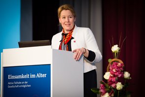Bundesministerin Franziska Giffey, Bundesministerin Franziska Giffey, eine Frau mittleren Alters mit hochgestecktem blondem Haar hält eine Rede an einem Pult. Am Pult ist ein Plakat angebracht mit der Aufschrift "Einsamkeit im Alter". Klick öffnet eine vergrößerte Ansicht.