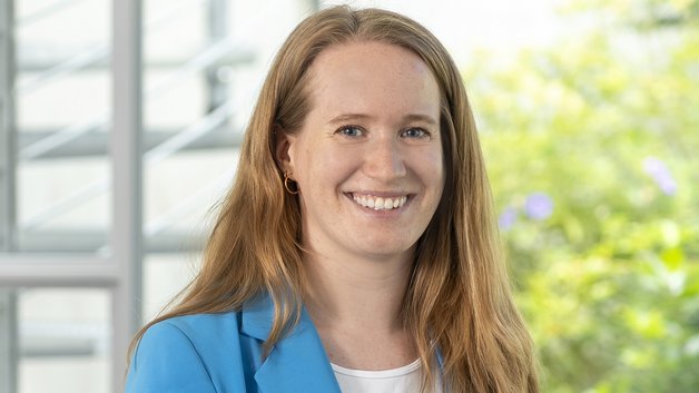 ©BAGSO/Sachs Protrait Marie Großmann: Junge Frau mit langen braunen Haaren. Sie trägt ein weißes T-Shirt und darüber einen hellblauen Blazer. Sie lächelt mit strahlenden Augen.