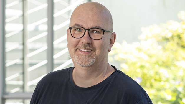 © BAGSO/Sachs Portrait Klemens Lenz: Mann mittleren Alters mit Glatze, Brillenträger. Er trägt ein schwarzes T-Shirt. Er schaut lächlelnd.