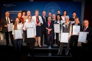 Eine Gruppe von Menschen stehen auf einer Bühne. Einige halten gerahmten Urkunden in der Hand. In der Mitte der Gruppe stehen Bundesministerin Giffey, BAGSO-Vorsitzende Franz Müntefering und Prof. Ursula Lehr. Klick öffnet eine vergrößerte Ansicht.