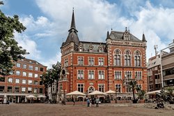 Oldenburger Rathaus: Ein altes Gebäude aus rotem Ziegel, rechts ein Turm mit Spitze. Davor ein Marktplatz und links daneben ein Bau aus den 60iger Jahren.