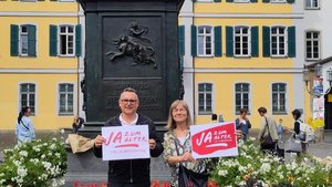 ©BAGSO Ein Mann und eine Frau stehen vor einem Denkmal, von dem nur der Sockel zu sehen ist.  Sie halten beide jeweils ein Schild in der Hand mit der Aufschrift "Ja zum Alter!"