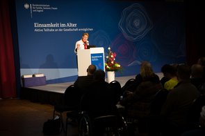 Bundesministerin Franziska Giffey, Bundesministerin Franziska Giffey, eine Frau mittleren Alters mit hochgestecktem blondem Haar hält eine Rede an einem Pult. Am Pult ist ein Plakat angebracht mit der Aufschrift "Einsamkeit im Alter". Klick öffnet eine vergrößerte Ansicht.