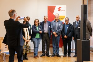 Ein Mann mittleren Alters fotografiert eine Gruppe von Personen unterschiedlichen Alters vor einem Banner mit der Aufschrift BAGSO. Klick öffnet eine vergrößerte Ansicht.