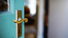 ©istock.com/brazzo Ausschnitt einer türkisfarbenen Tür mit goldfarbener Klinke. Die Tür ist geöffnet und man erhält einen Blick in eine Wohnung.