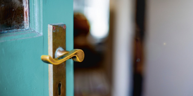 ©istock.com/brazzo Ausschnitt einer türkisfarbenen Tür mit goldfarbener Klinke. Die Tür ist geöffnet und man erhält einen Blick in eine Wohnung.