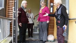 © Forum Gemeinschaftliches Wohnen Drei alte Frauen stehen vor dem Eingang einer Haustür. Eine im Haus. Sie unterhalten sich lachend.