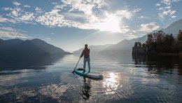 ©iStoch_swissmediavision Eine Frau von hinten. Sie macht gerade Standup-Paddling auf einem See, der von Bergen umgeben ist.