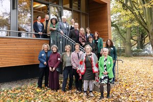 ©BAGSO_Seng A group of people of different ages are standing in front of and on a staircase for a group photo. The event building with a wooden and glass façade can be seen in the background. Klick öffnet eine vergrößerte Ansicht.